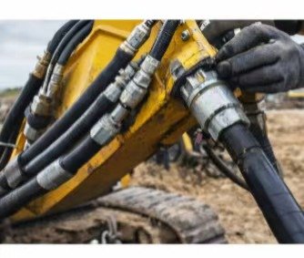 Field mechanic inspecting high-pressure hydraulic hose fittings on a yellow heavy excavator arm, demonstrating typical earthmoving machinery applications.